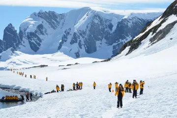 Exploradores caminando en la Isla Cuverville, Antártida, rodeados de nieve, montañas y pingüinos en un paisaje polar impresionante.