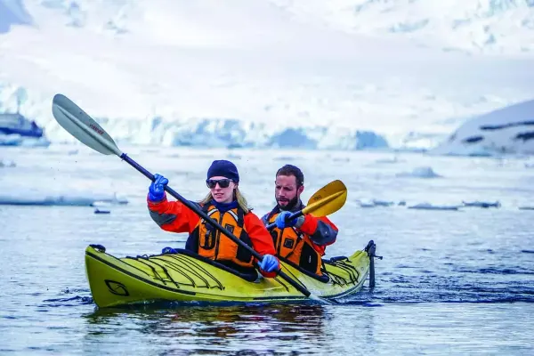 Turista en kayak navegando entre icebergs en la Antártida, rodeado de un paisaje ártico impresionante y aguas tranquilas.
