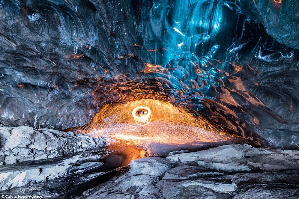 Efecto mágico: un guía turístico arroja chispas de fuego al suelo dentro del glaciar Vatnajökull de Islandia, mientras está rodeado de ondas de hielo.
